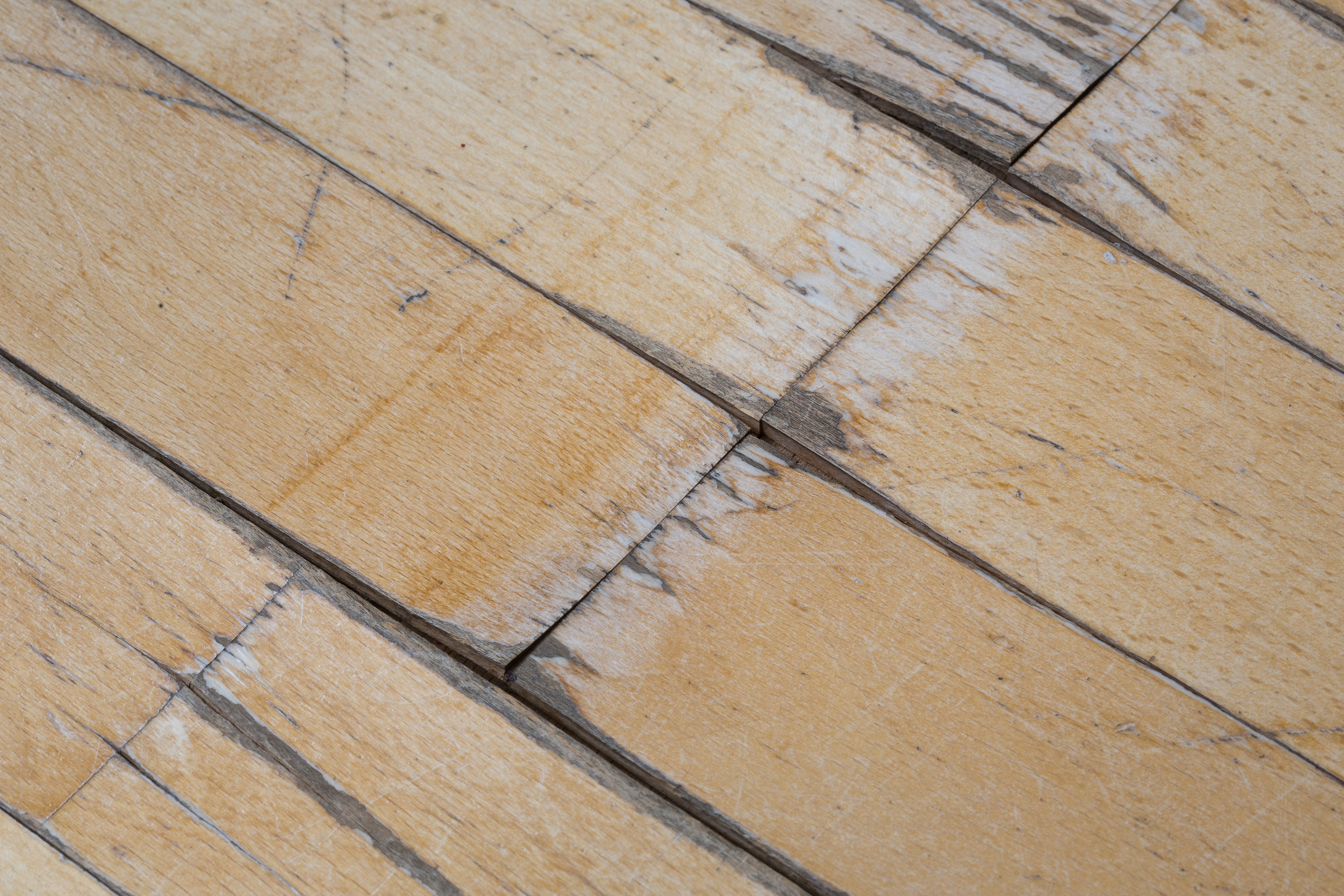 Close-up of deformed and scratched hardwood flooring caused by water exposure, highlighting the importance of proper subfloor preparation and moisture control for long-lasting floor installations. Learn more about our expert flooring services at Veteran Flooring LLC.