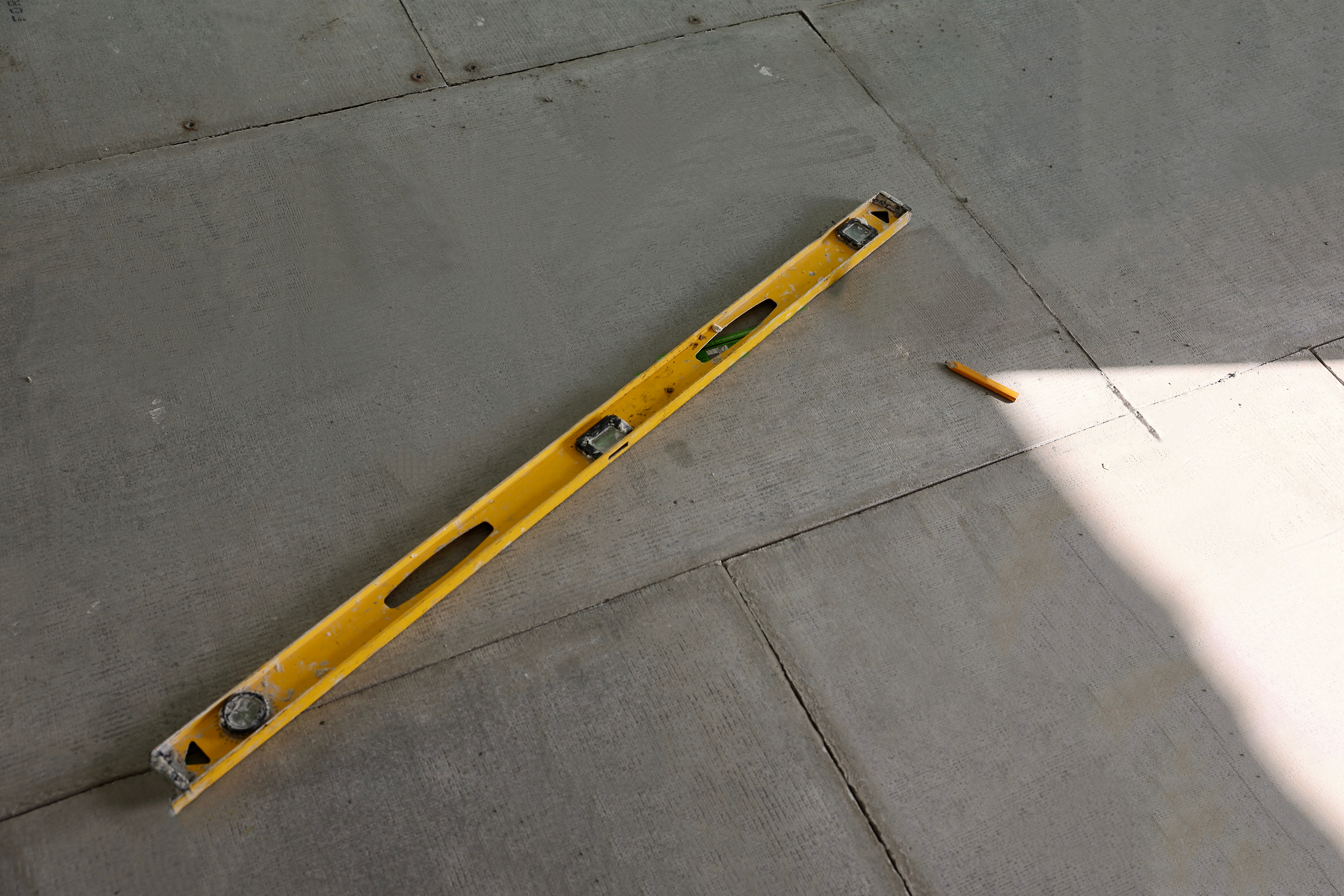 Close-up of a cement subfloor with a pencil and level, illustrating the importance of ensuring a level subfloor for successful flooring installation. Discover expert subfloor preparation tips and services at Veteran Flooring LLC.